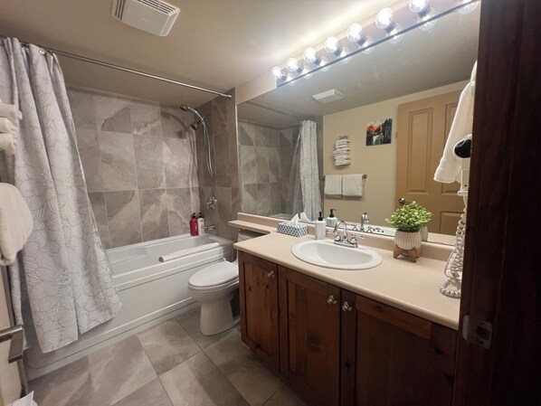 Een badkamer met een bad, toilet en wastafel. Boven de spiegel hangen verlichtingselementen, en aan de muur bevinden zich handdoeken.