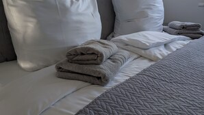 A neatly made bed with white and gray bedding, a quilted gray blanket, and folded towels. - Charming vacation apartment in the heart of the northern Black Forest (Haiterbach)