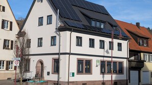 A white building with solar panels on the roof, a sign indicating a 30 km/h speed limit, and a public water fountain. - Charming vacation apartment in the heart of the northern Black Forest (Haiterbach)