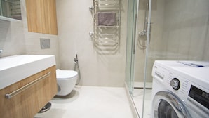Une salle de bain moderne avec une douche à parois de verre, un lave-linge encastré et des toilettes.