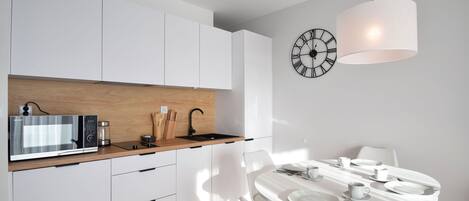 Una cocina moderna con armarios blancos, encimera de madera y comedor con mesa y sillas blancas.