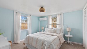 Un dormitorio con una cama, dos mesitas de noche, una ventana con cortinas e instalación de aire acondicionado.