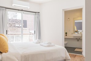 A hotel room with a bed, a window with curtains, a bathroom with a sink and mirror, and a view of the outside. -  MOT SohoGlam - Lux Aparts Palermo Soho (Buenos Aires)