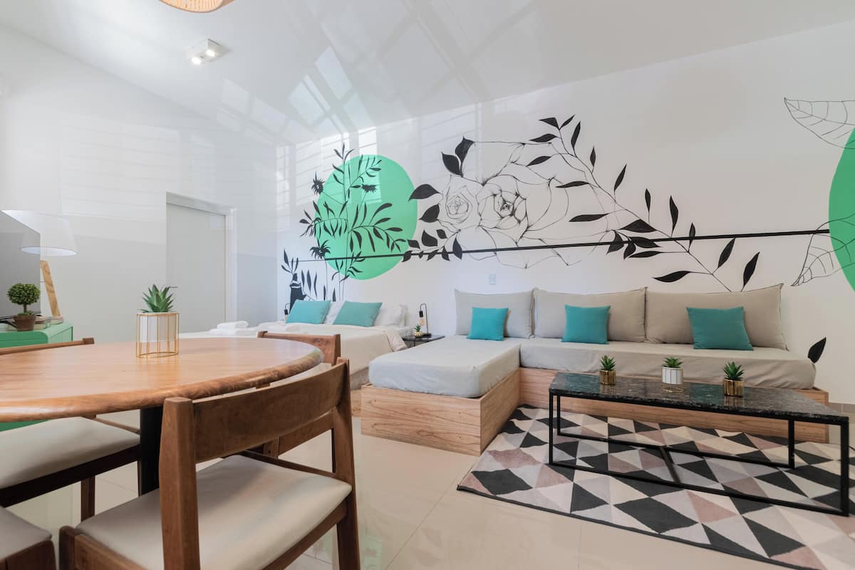 A modern living room with a wooden dining table, a sofa set, and a decorative wall with abstract art.
