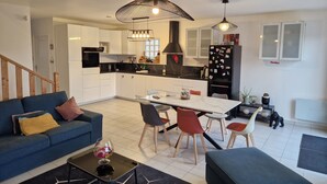 Una cocina moderna con armarios blancos, un refrigerador negro y una zona de comedor con mesa y sillas.