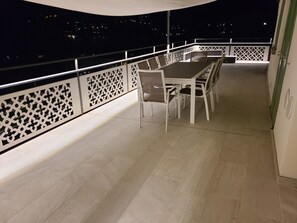 A balcony with a dining table and chairs, a decorative railing, and a view of the city at night. - Villa "La Gabbianella" Overview in Moltrasio, Como (Moltrasio)