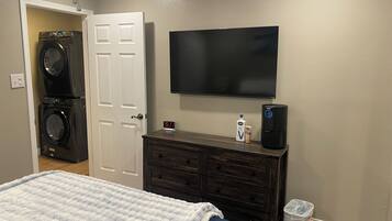 A bedroom with a bed, a dresser, a TV, a washing machine, and a trash can.