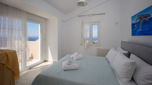 A hotel room with a bed, a painting of dolphins, a window with curtains, and a view of the sea. - Blue Hills Villas by Estia Purple 1 (Malevizi)