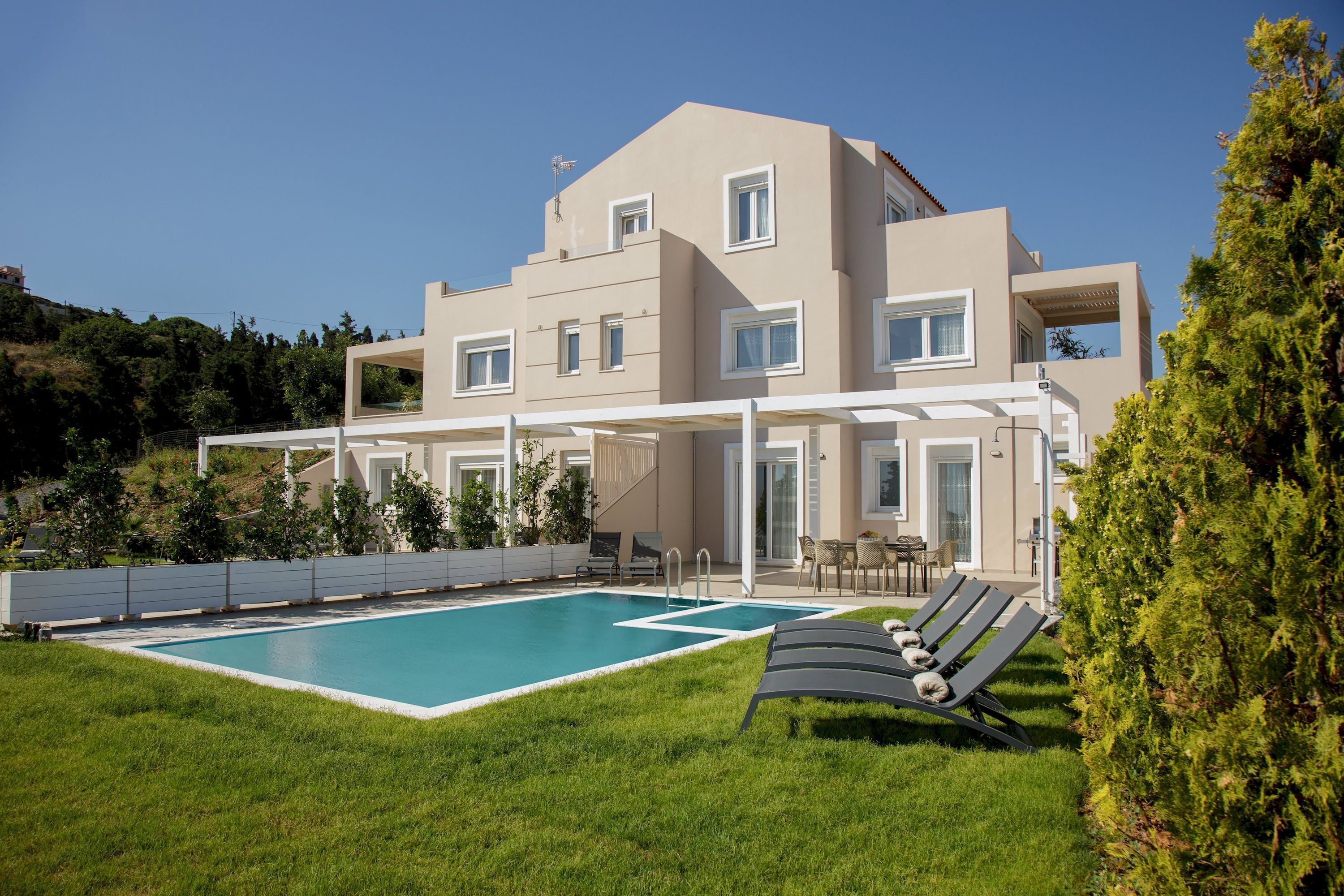Ein modernes, zweistöckiges Haus mit Schwimmbad, Außenbereich zum Sitzen und einer überdachten Terrasse.