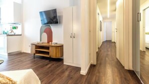 Un salon moderne doté d’un téléviseur à écran plat fixé au mur, d’un meuble de rangement en bois et d’un couloir menant aux autres pièces.