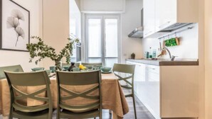 Un coin repas avec une table dressée pour quatre personnes, des chaises et un vase rempli de fleurs.