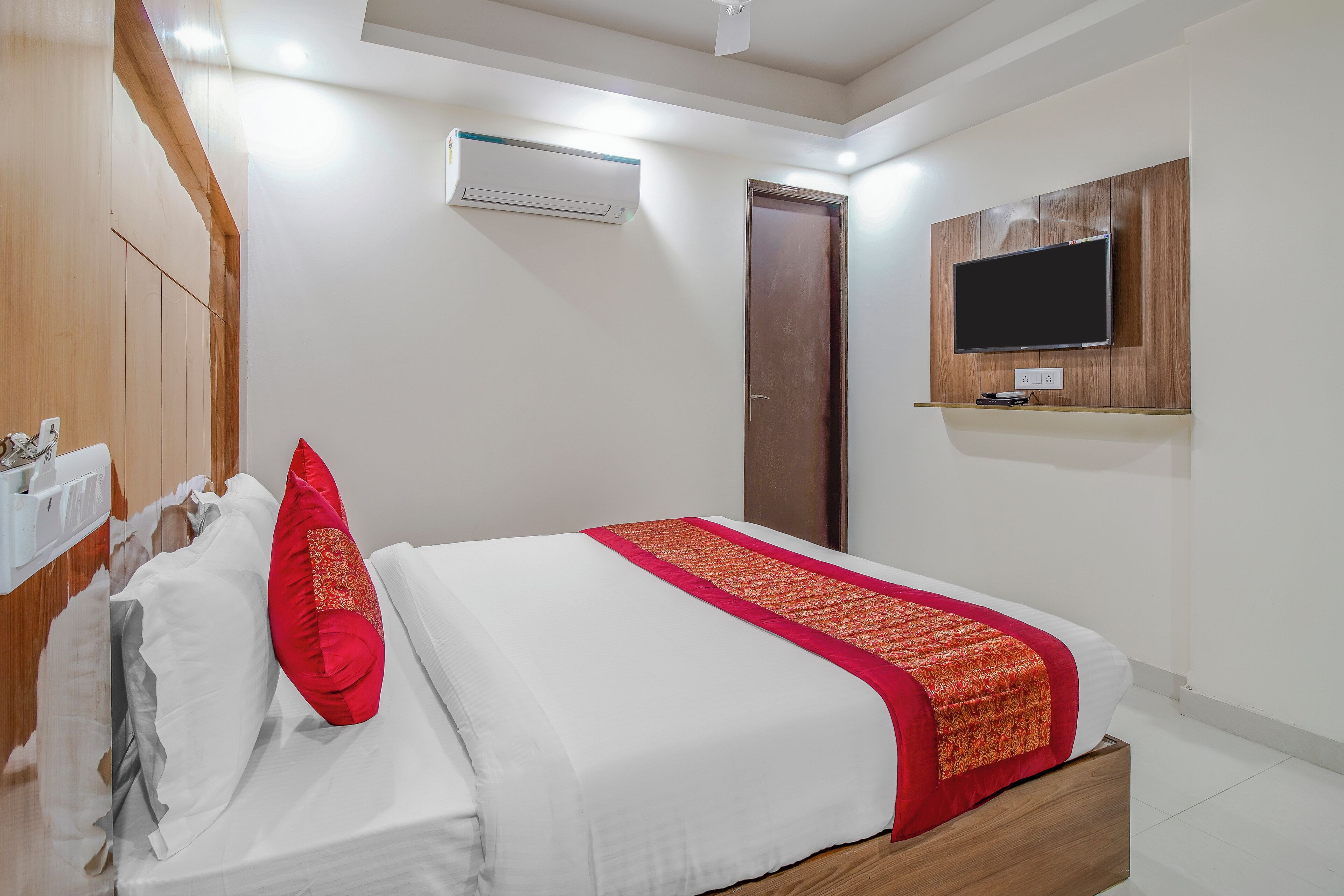 A bedroom with a bed, a TV mounted on the wall, and an air conditioning unit.
