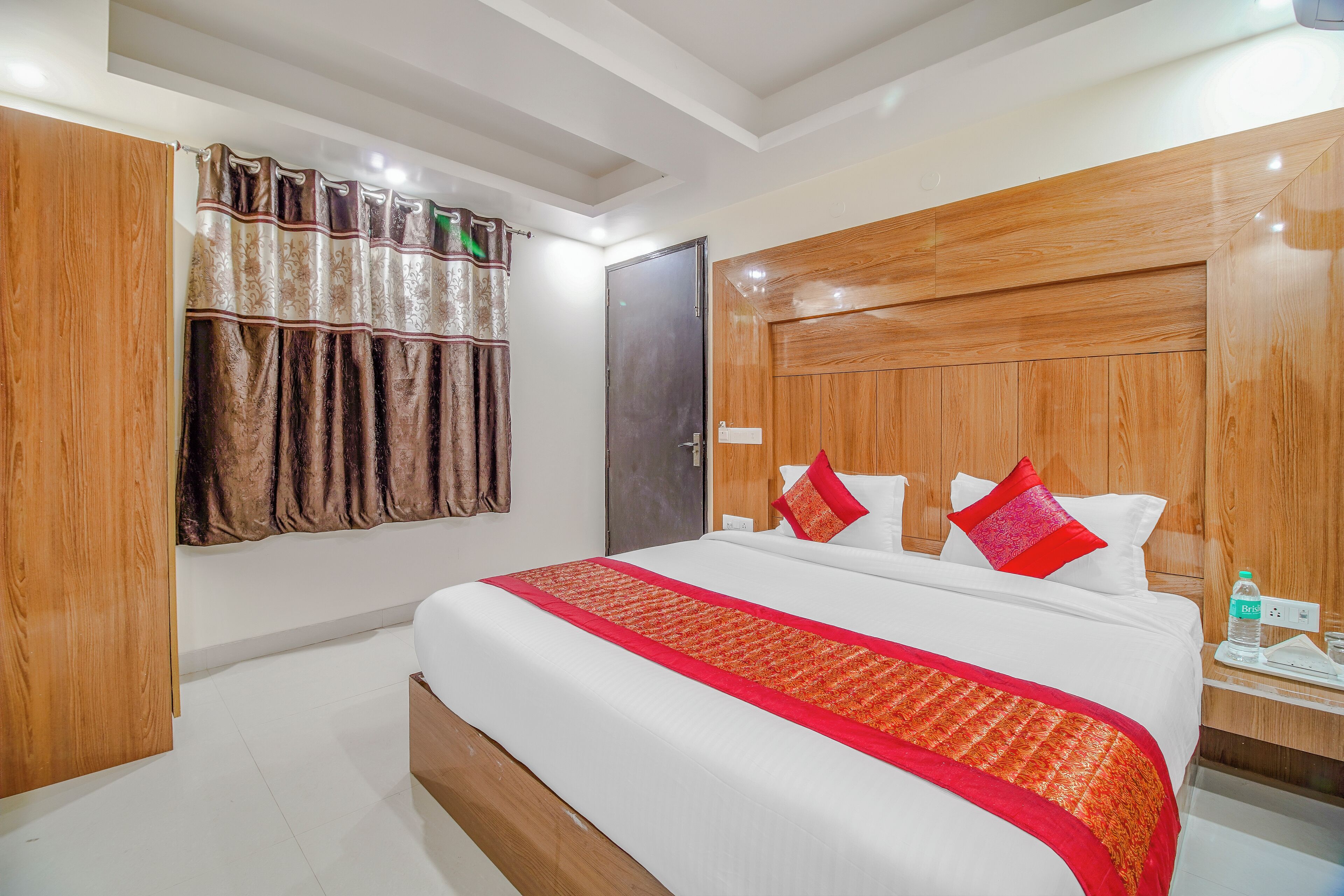 A hotel room with a large bed, wooden headboard, and a red and gold bedspread.