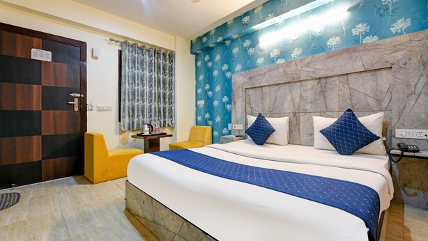 A hotel room with a large bed, a small table, a chair, and a ceiling fan. - Hotel The white Sand suites (New Delhi)