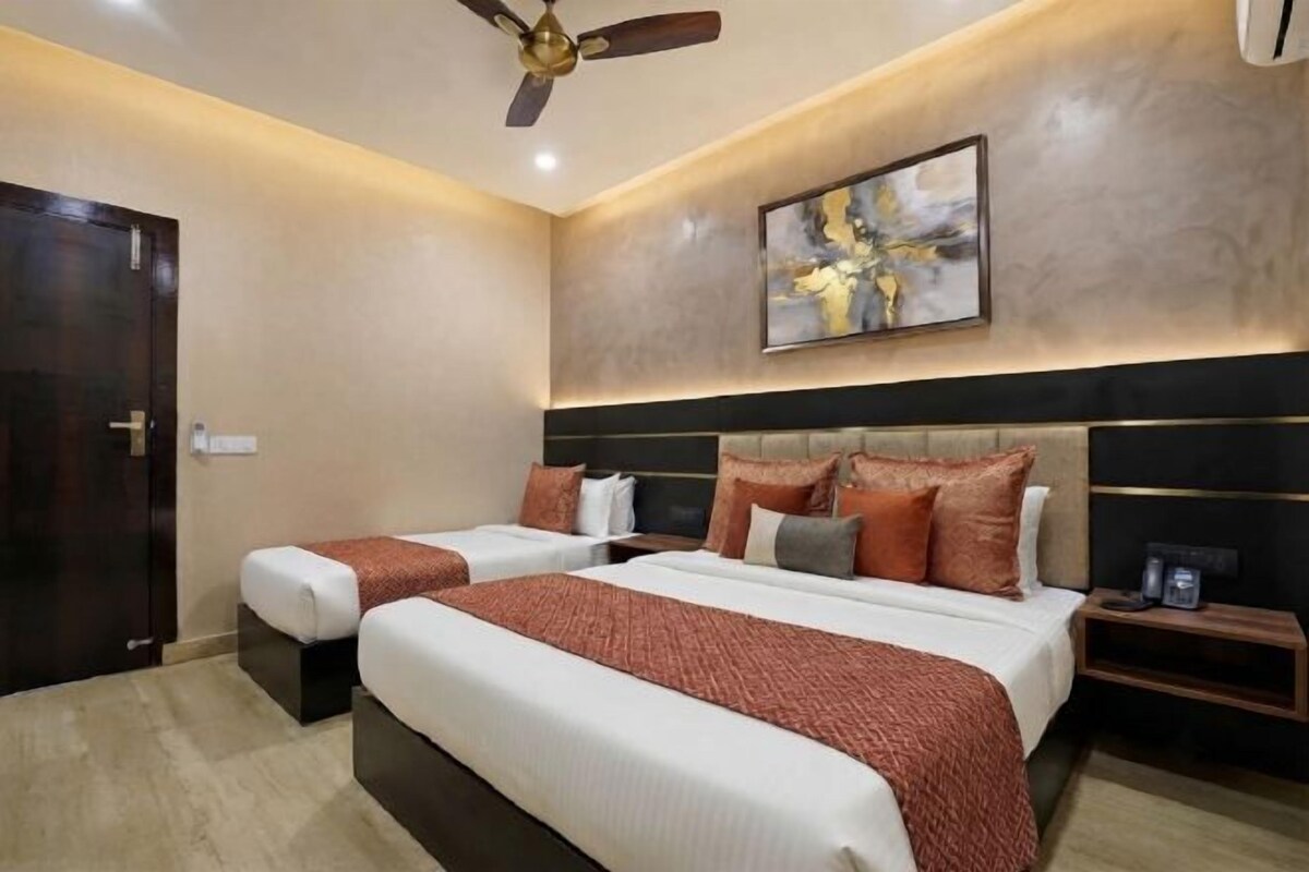 A hotel room with two beds, a ceiling fan, a painting on the wall, and a nightstand with a lamp.