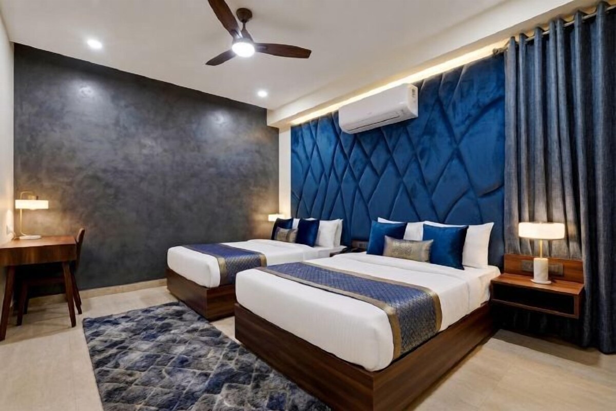 A hotel room with two beds, a ceiling fan, a desk, and a large window with curtains.