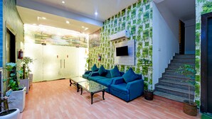 A modern living area with a blue sofa, a glass coffee table, and potted plants. - Hotel The white Sand suites (New Delhi)
