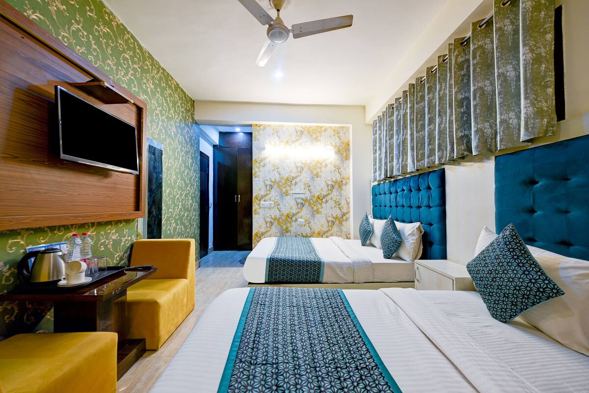 A hotel room with two beds, a TV mounted on the wall, a ceiling fan, and a bathroom visible through an open door.