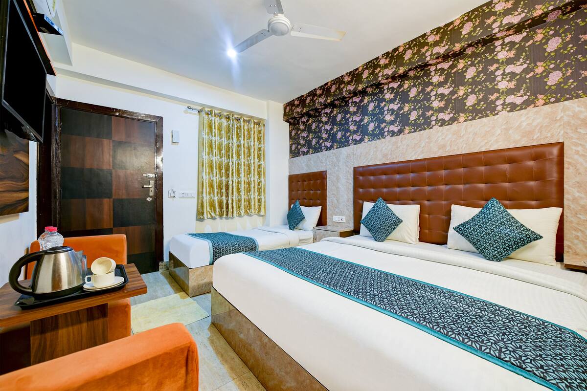 A hotel room with two beds, a wooden desk with a kettle and cups, and a ceiling fan.