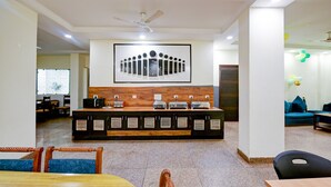 A reception area with a wooden counter, seating, and a large clock on the wall. - Hotel The white Sand suites (New Delhi)