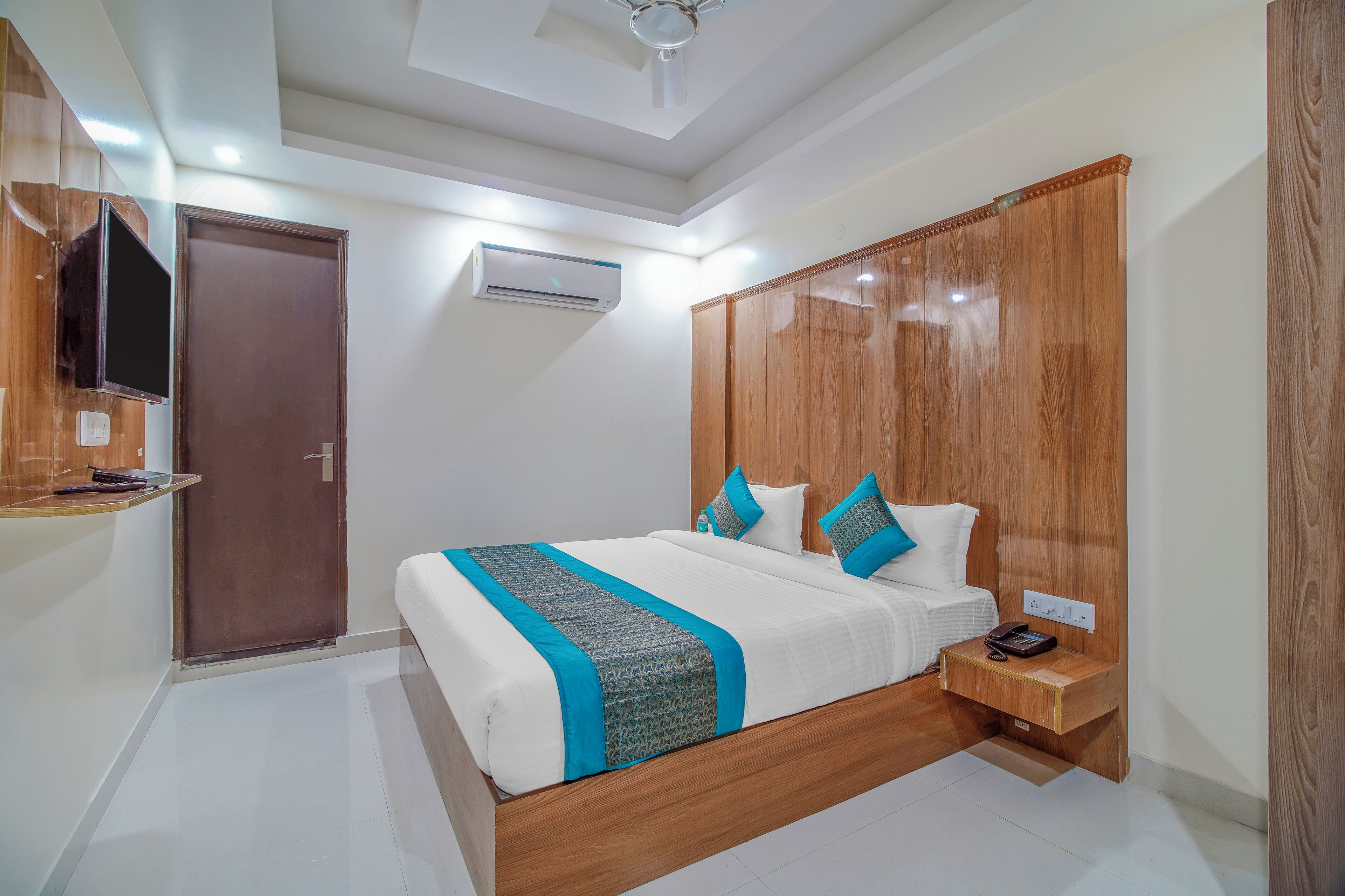 A bedroom with a wooden bed frame, a TV mounted on the wall, and an air conditioning unit.