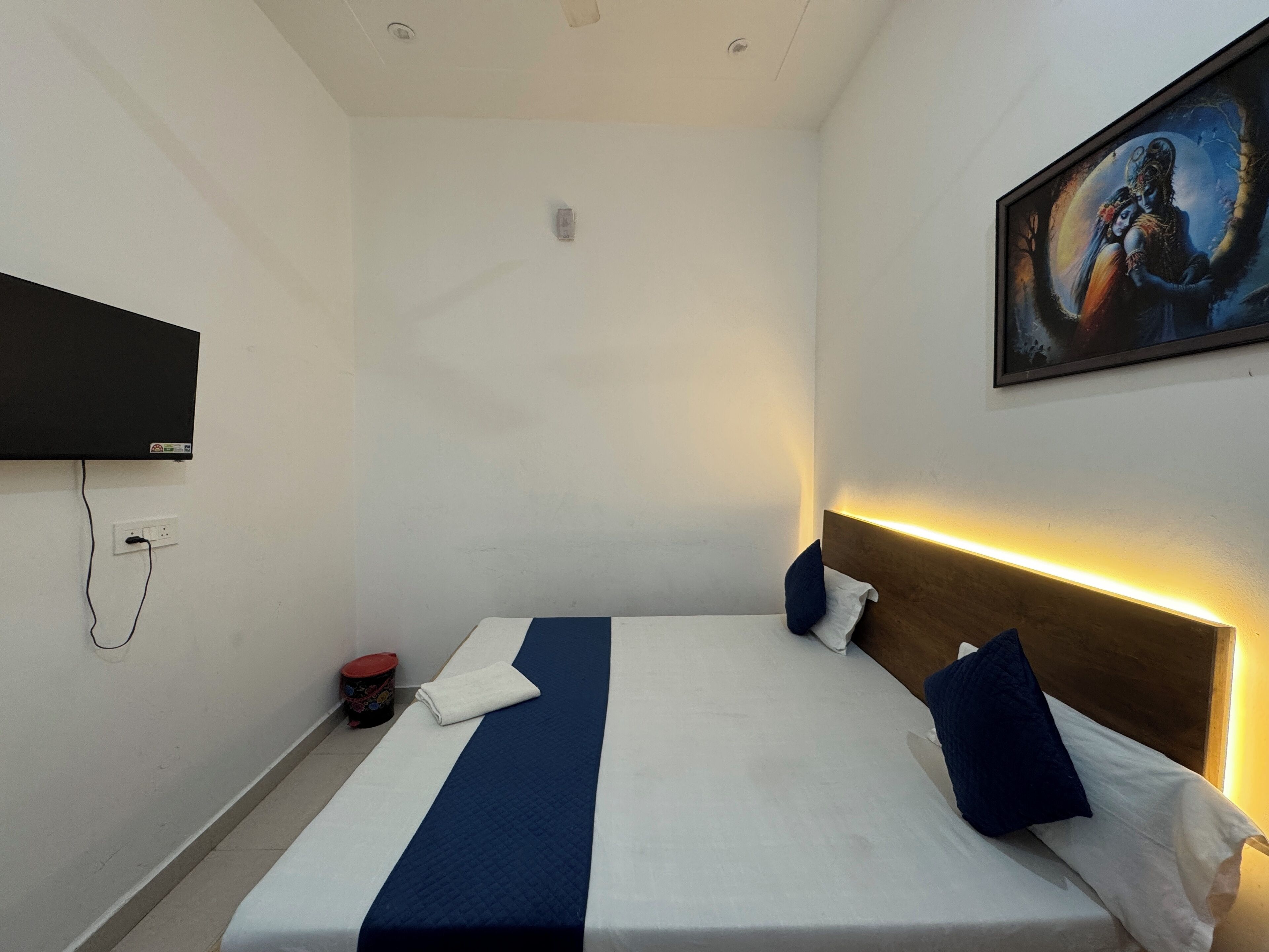 A hotel room with a bed, a flat-screen TV mounted on the wall, and a painting above the bed.
