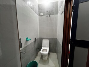 A small, compact bathroom with a toilet, a shower, and a grab bar. - Shree Radha Vallabh Palace- 800 m from prem mandir (Vrindavan)
