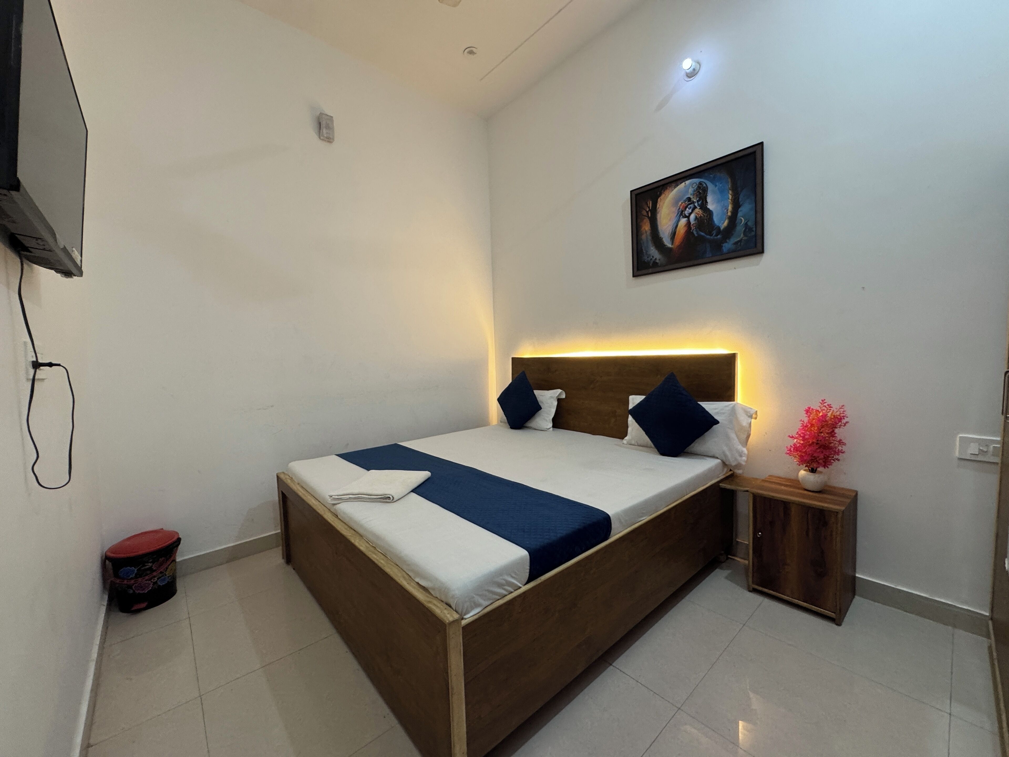 A neatly arranged bedroom with a wooden bed, a bedside table with a vase, and a painting on the wall.