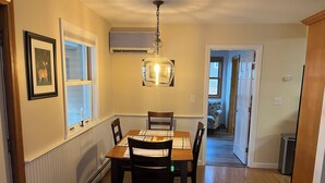 A dining area with a wooden table and chairs, a pendant light, and a framed picture on the wall.