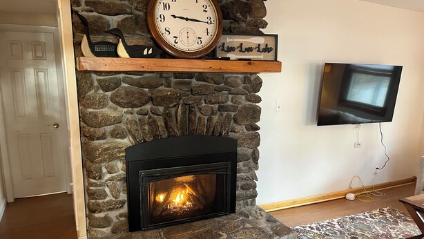 A stone fireplace with a clock above it, a television mounted on the wall, and a wooden door.