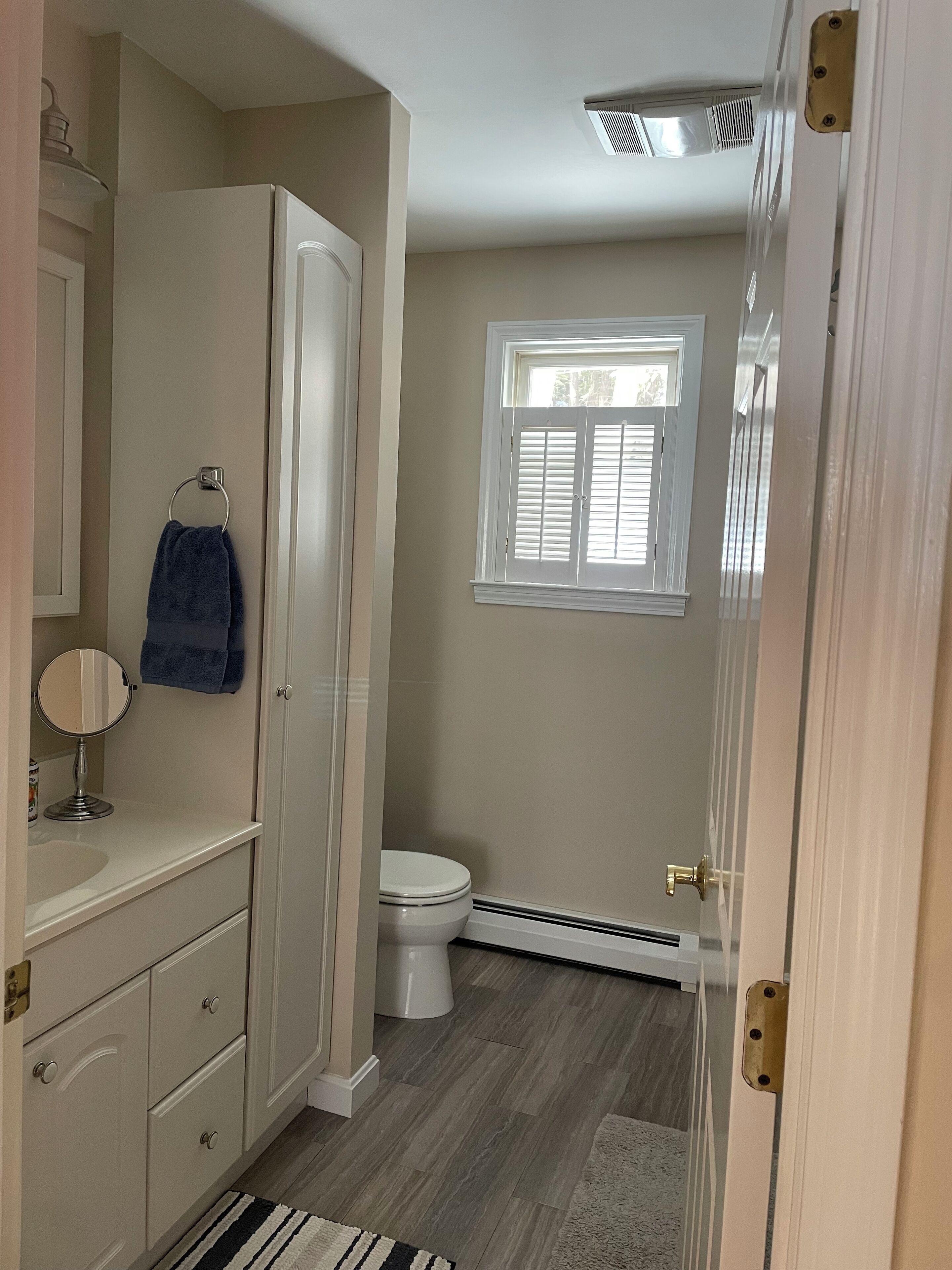 A bathroom with a toilet, a sink, a mirror, a towel rack, and a window.