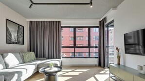 Ett modernt vardagsrum med en hörnsoffa, ett soffbord, en tv och ett stort fönster med utsikt över staden.