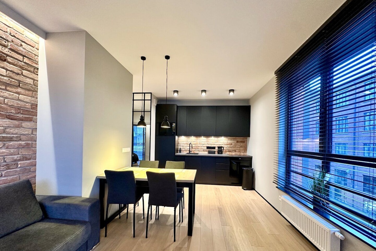 A modern kitchen with dark cabinets, a brick accent wall, and a dining area with a table and chairs.