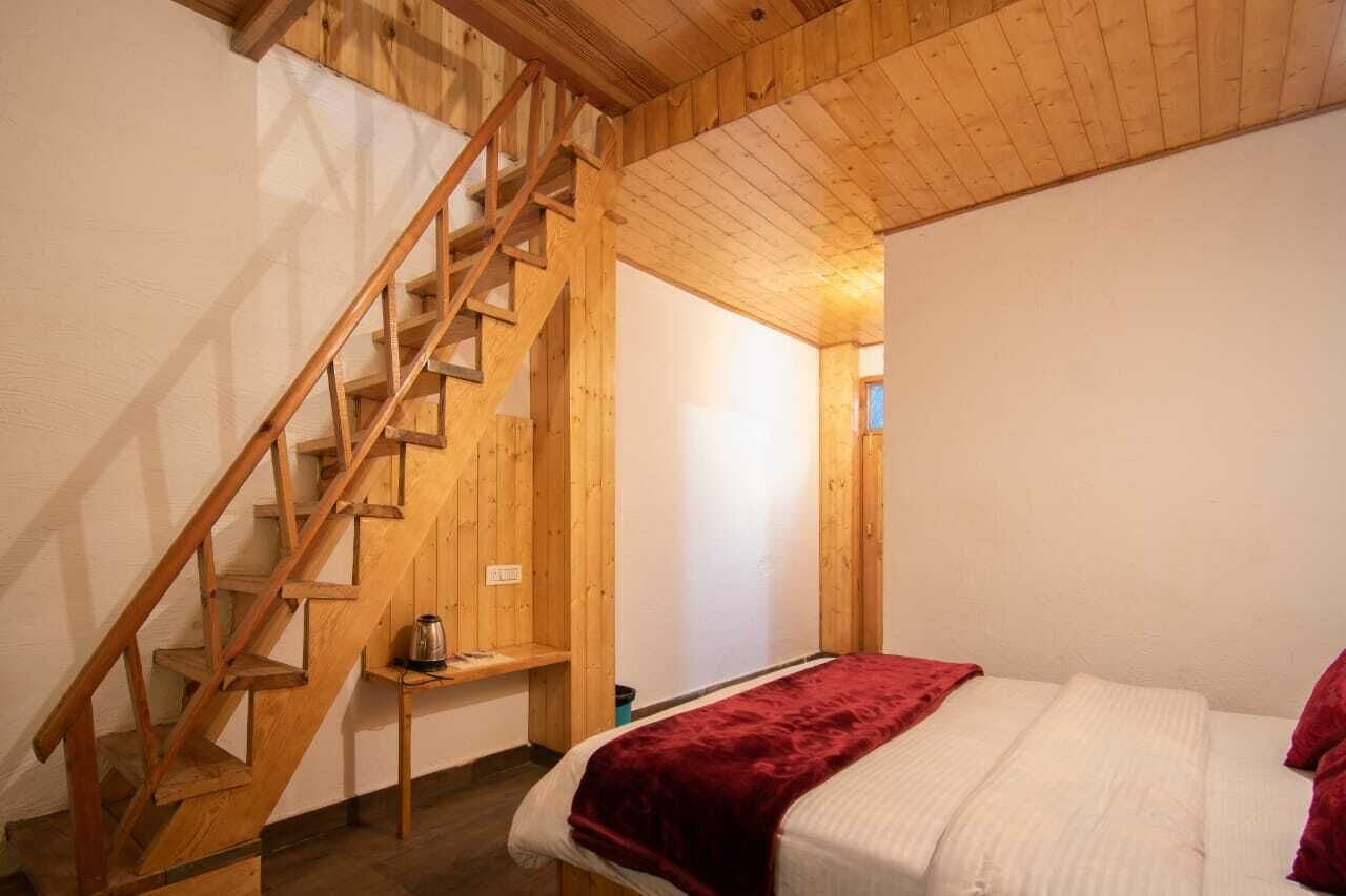 Un escalier en bois mène à une chambre à coucher où se trouve un lit recouvert d’une couverture rouge.