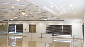 A spacious, well-lit hotel lobby with a polished marble floor, large windows with blinds, and a modern ceiling design.