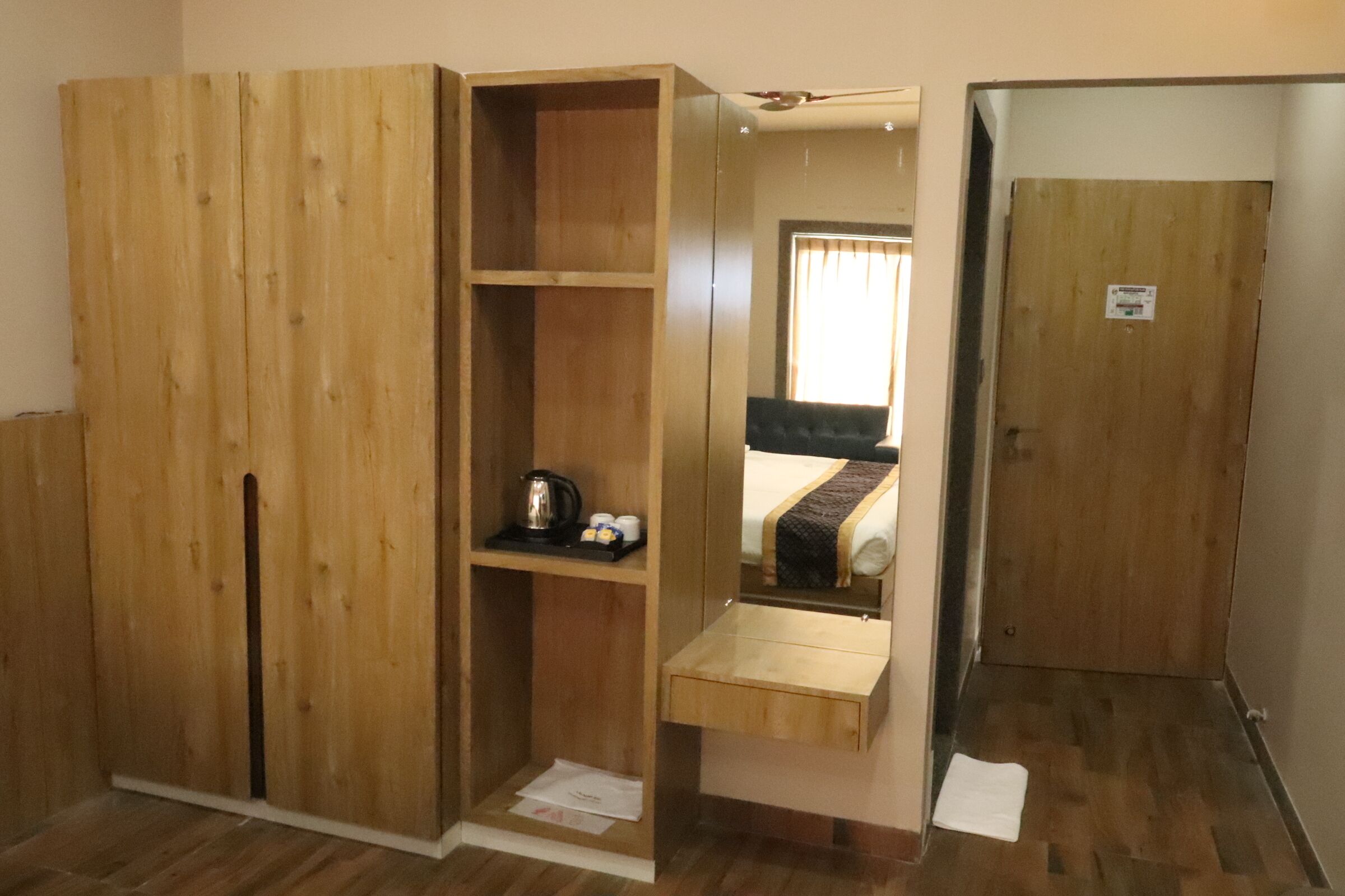Una habitación con un armario de madera, una pequeña estantería con una tetera y una cama con una manta.