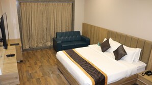 A hotel room with a wooden bed, a dark blue sofa, a wooden nightstand, and a television on a wooden stand.