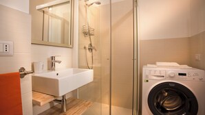 A modern bathroom with a glass-enclosed shower, a white sink, and a front-loading washing machine. - STUDIO BIJOUX (Verona)