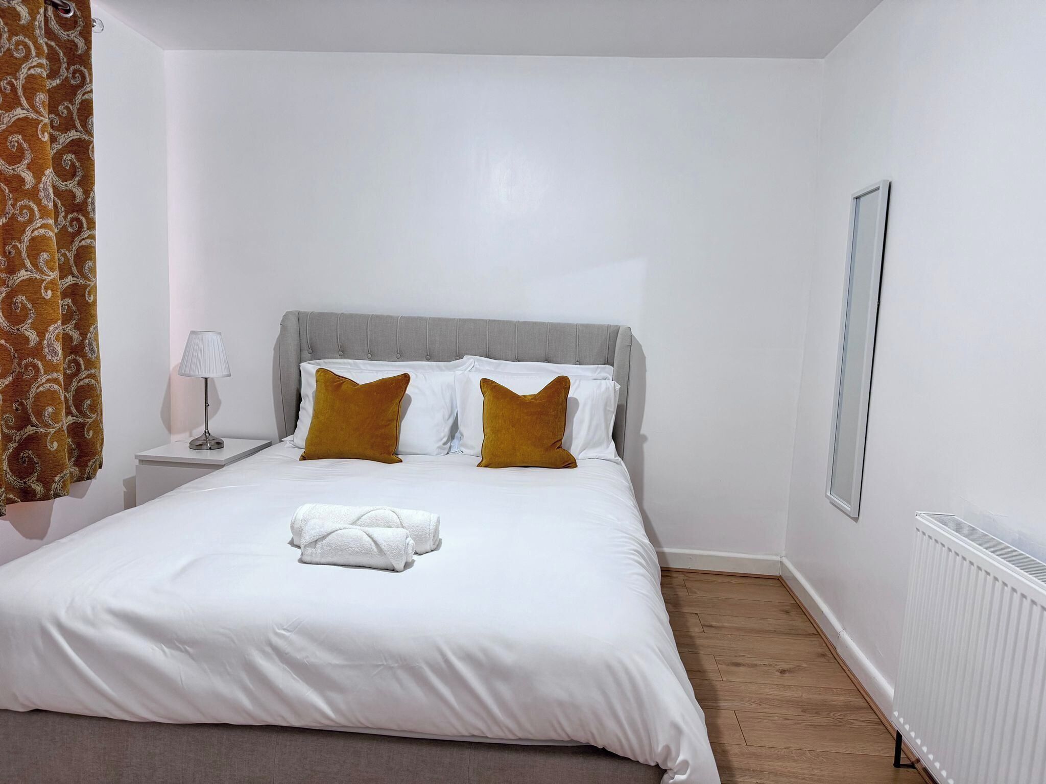 A neatly made bed with white linens, two mustard-colored pillows, and a white towel on the bed.