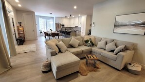 A modern living room with a sectional sofa, a coffee table, and a dining area with chairs. - Spacious 3 bedroom condo in the heart of Mount Orford's nature (Orford)