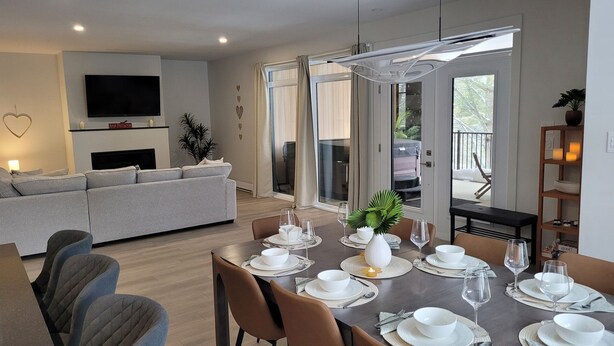 A modern living room with a dining area, a sofa, a TV, and a balcony with a view. - Spacious 3 bedroom condo in the heart of Mount Orford's nature (Orford)
