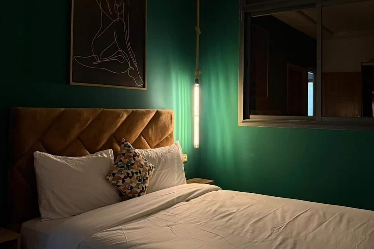 Un lit bien fait, avec du linge de lit blanc, une tête de lit marron et un coussin à motifs géométriques.