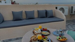 A rooftop terrace with a sofa and dining table set with breakfast. - Playa Surf House (Aourir)