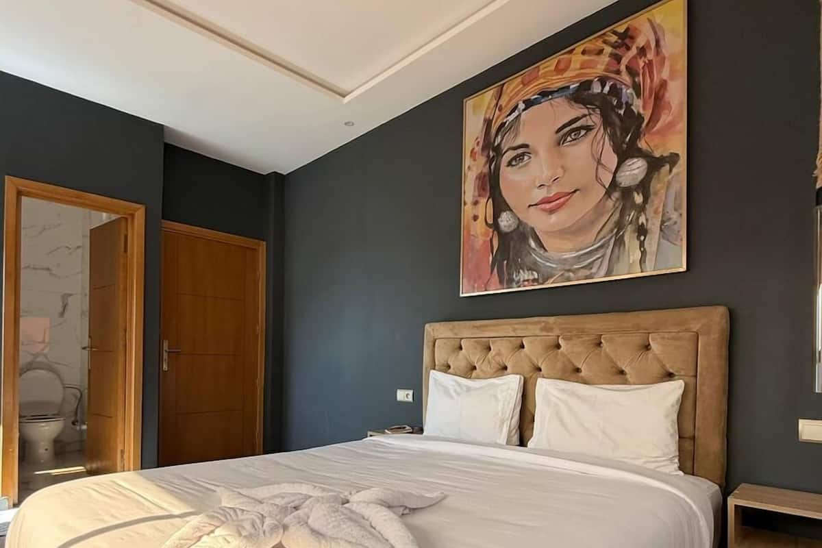 Une chambre à coucher avec un grand lit, une tête de lit en bois, un tableau au mur et une porte en bois.