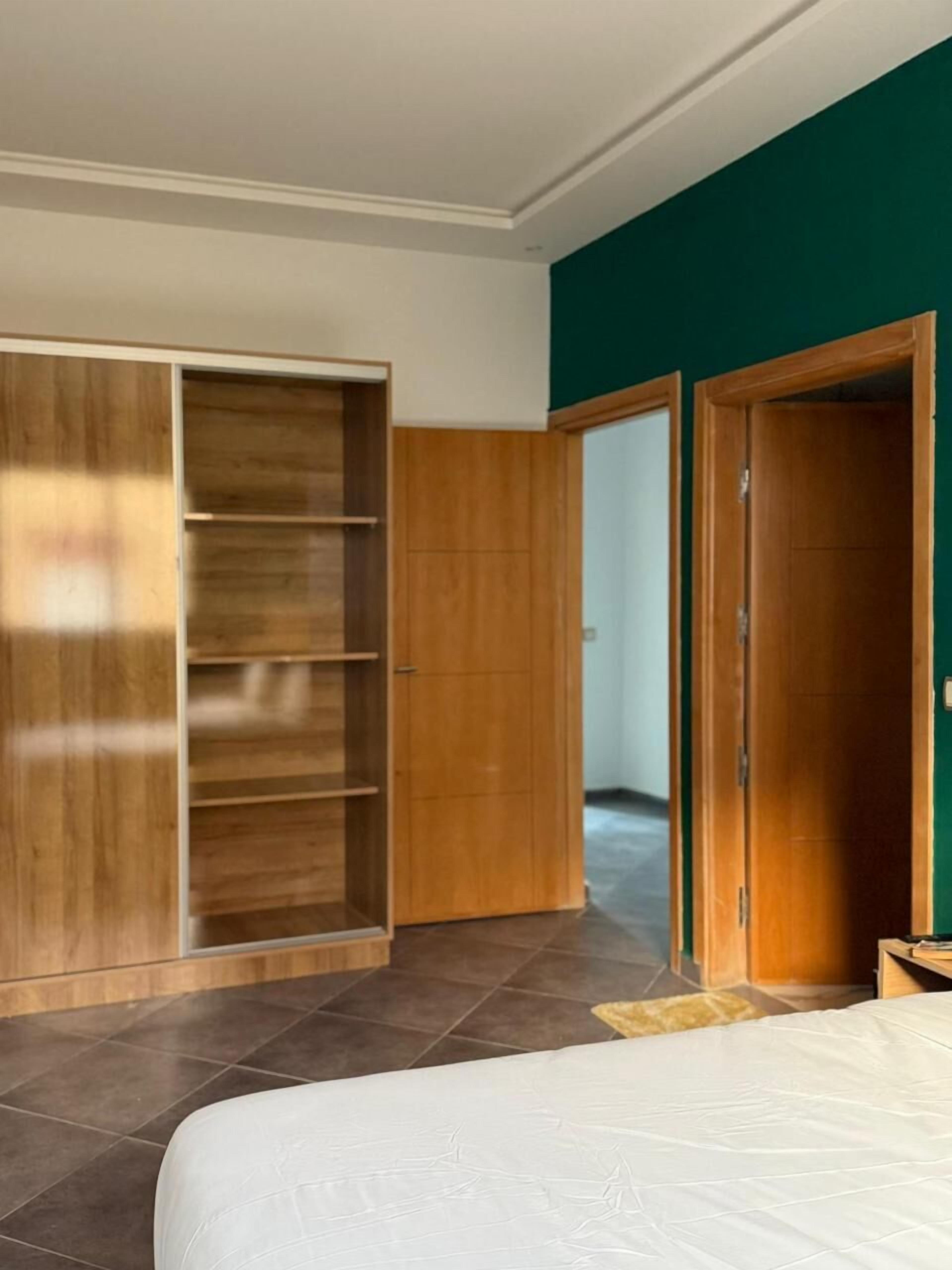A bedroom with a large wardrobe, a bed, and a green accent wall.