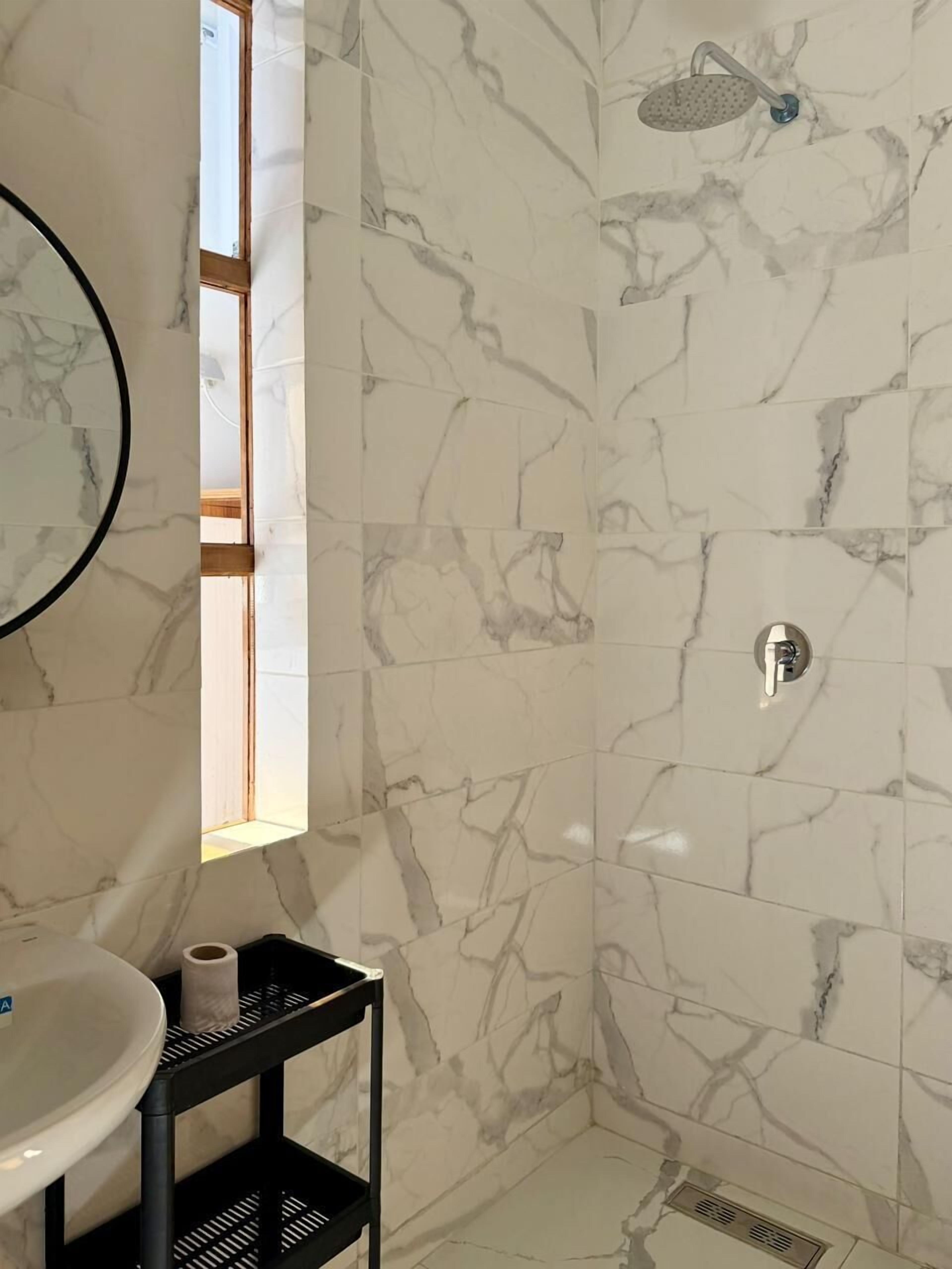 A bathroom with a marble wall, a shower, a sink, and a window.
