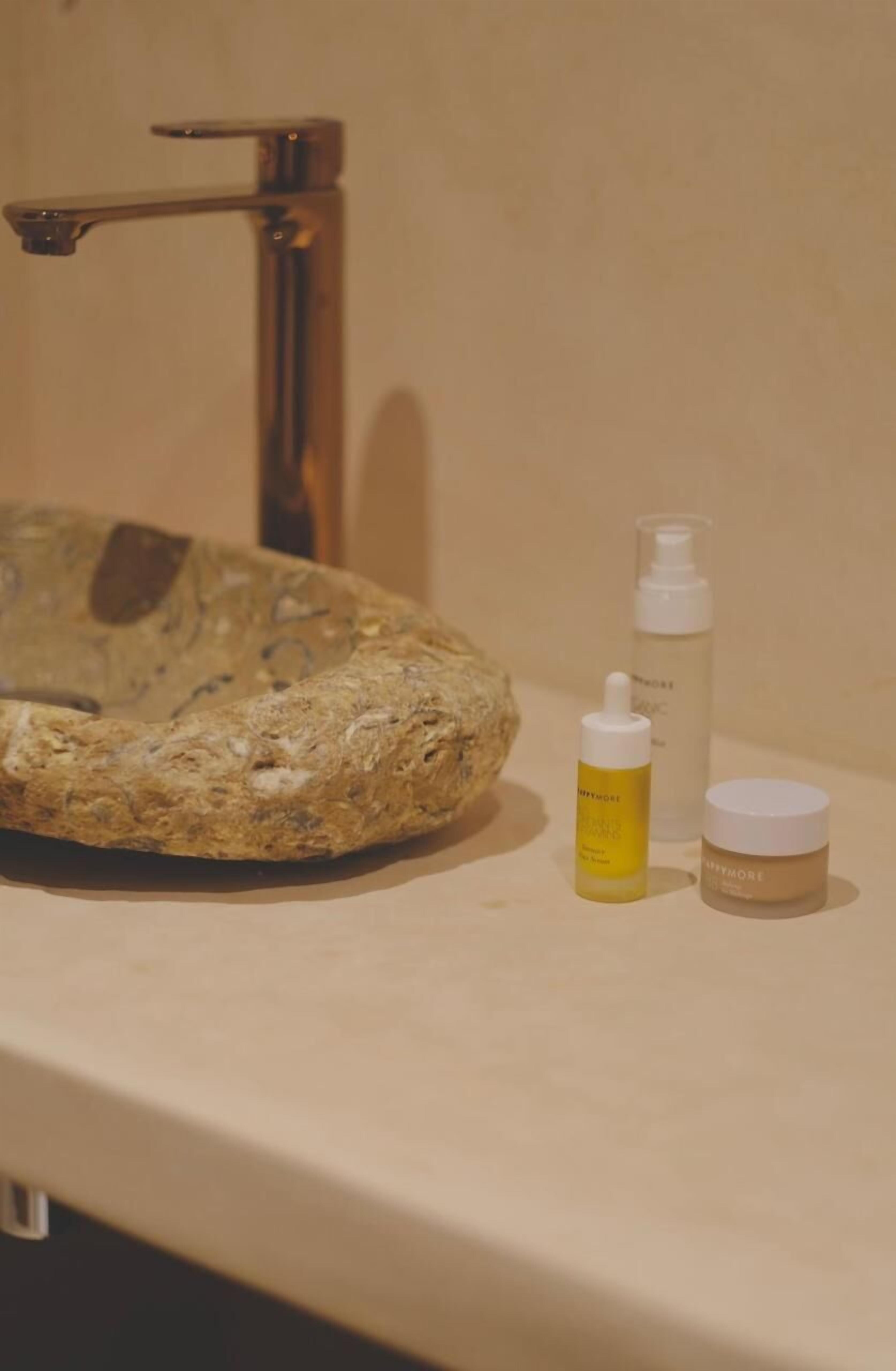 A bathroom sink with a unique stone basin, a faucet, and two skincare products on the counter.