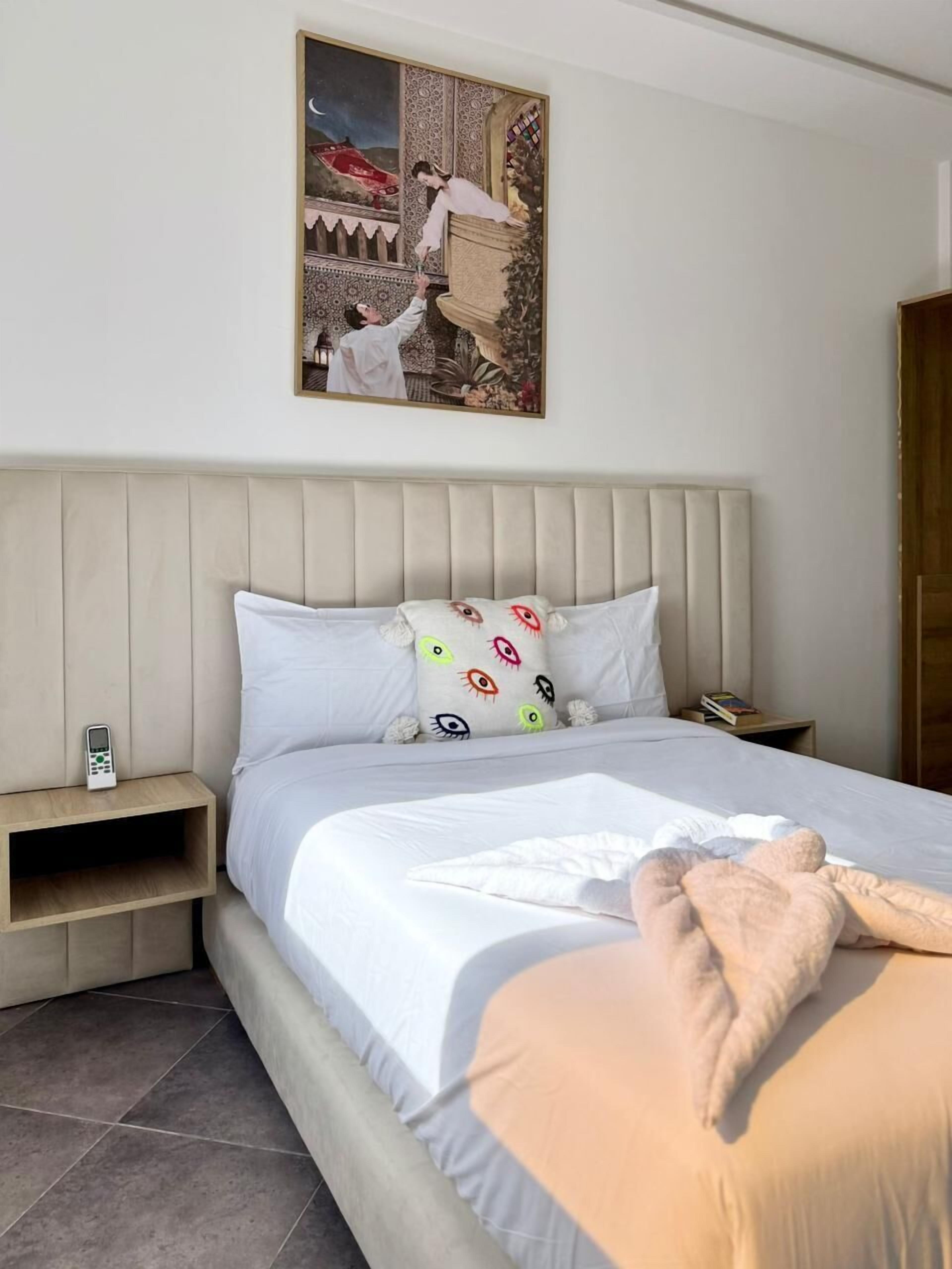 Un dormitorio con cama, mesita de noche, cuadro colgado en la pared y puerta de madera.