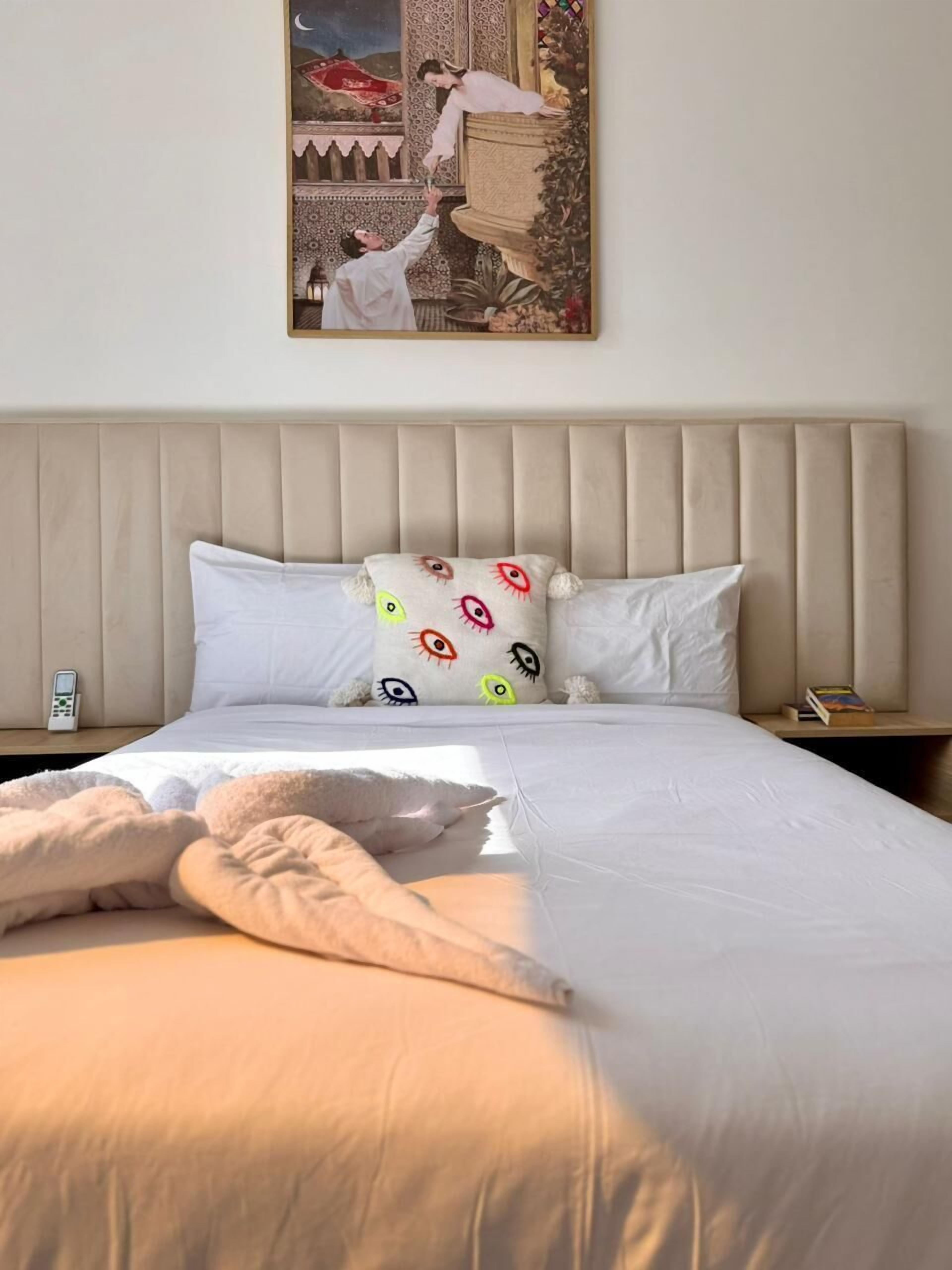 A hotel room with a large bed, a headboard, and a painting on the wall.