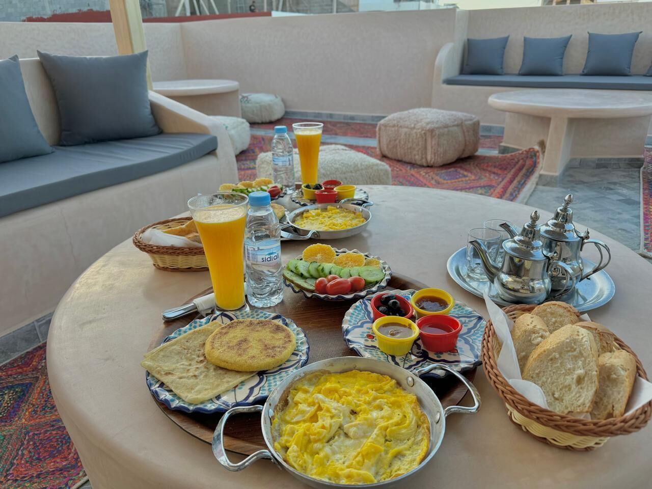 A breakfast setting with various dishes, drinks, and a teapot on a round table.